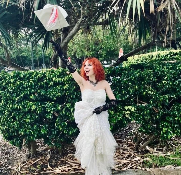 happy teenage girl with bright red hair wearing a white dress and black gloves